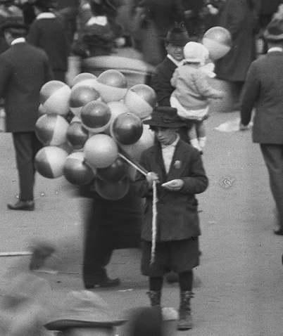 Young boy in crowd selling balloons.