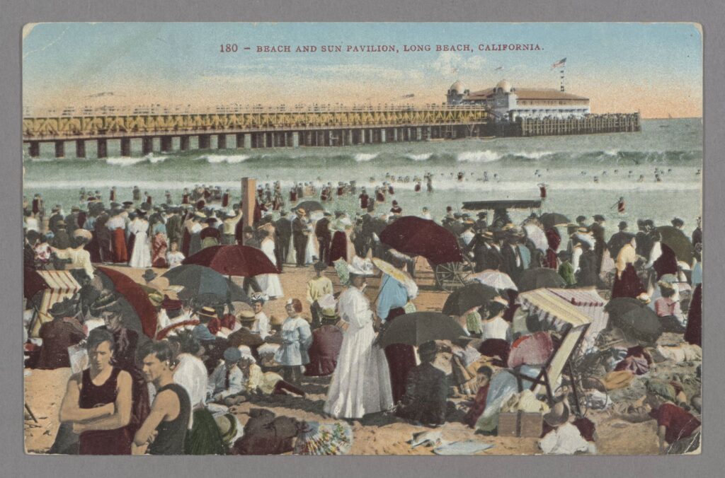 Color postcard of well-dressed crowds on the beach at Long Beach, with pier in background, circa 1905